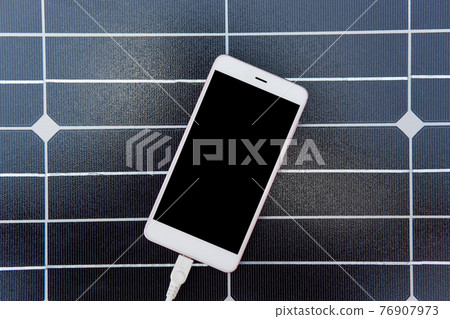 Photo of modern device charging via USB, lying on solar power panel, top view of smartphone with white cabel connected to it over dark background, sustainable resources. Alternative sources of energy. 76907973