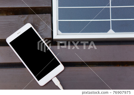 Image of light smartphone lying on brown bench, solar pannel installed inside, mobile phone switched off, having black screen, modern device being connected to USB cable. Modern technologies concept. 76907975