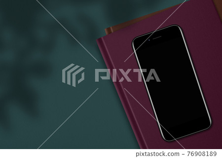 Top view of modern mobile phone with blank empty display on book or notepad, against green background with copy space aside for your promotional information Top view of modern mobile phone with blank empty display on book or notepad, against green background with copy space aside for your promotional information 76908189