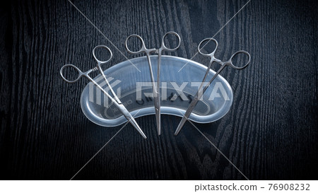 Hemostatic Forceps scissors lay flat on top of plastic equipment holder on a wooden table top, overhead view photograph. 76908232