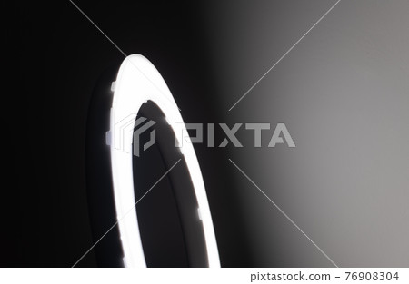 Large LED ring light in a studio room against empty walls side view and the very dark to bright light gradient wall effect. 76908304