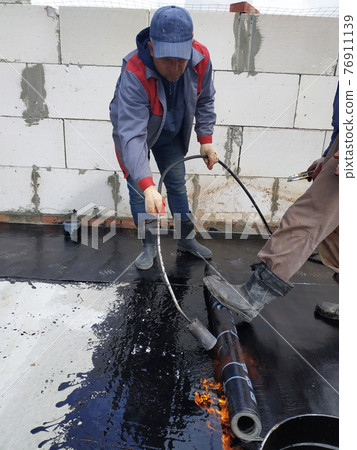 The master works with the assistant to work on the waterproofing of the surface. 76911139