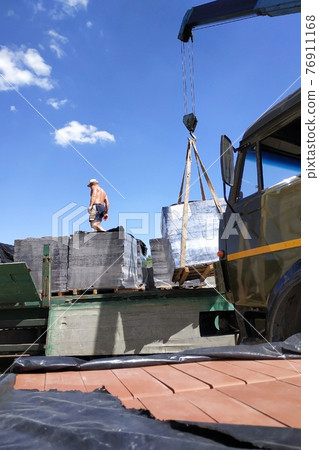 Workers unload pallets with bricks by means of the crane of automobile. Workers unload pallets with bricks by means of the crane of automobile. 76911168