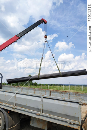 The truck crane in the field on the private land unloads the metal profile. The truck crane in the field on the private land unloads the metal profile. 76911218