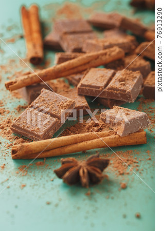 Chocolate broken into slices with cocoa powder and spices on a green background 76913290