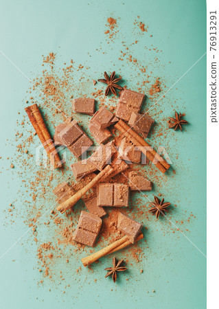 Dark chocolate slices with cinnamon and spices on a pastel green background. Dark chocolate slices with cinnamon and spices on a pastel green background. 76913291