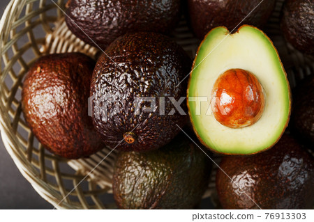 Ripe avocados in a basket on a black table, with a cut fruit and a stone. Ripe avocados in a basket on a black table, with a cut fruit and a stone. 76913303