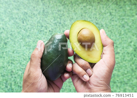 hand holding slice of avocado against green background  76913451