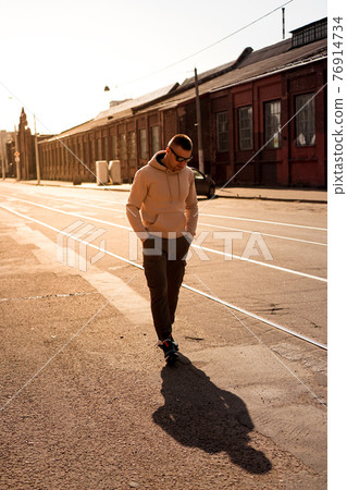 Hipster walking in the street with red brick wall building in summer day. Hipster walking in the street with red brick wall building in summer day. 76914734
