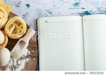 Tagliatelle with egg and flour on wooden board and notebook Tagliatelle with egg and flour on wooden board and notebook 76915839