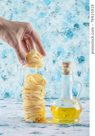 Male hand taking pasta nest from blue background Male hand taking pasta nest from blue background 76915919