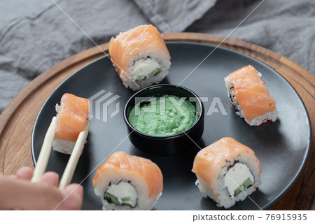 Salmon rolls with cream cheese in a black plate with wasabi sauce 76915935