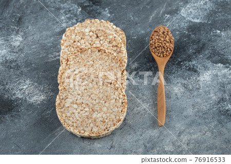 Puffed crispbread and wooden spoon of raw buckwheat on marble surface 76916533