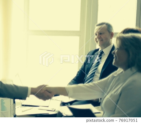 Smiling senior partners sitting together at a desk having a busi Smiling senior partners sitting together at a desk having a busi 76917051