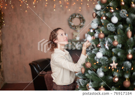 young woman decorating Christmas tree in her living room young woman decorating Christmas tree in her living room 76917184
