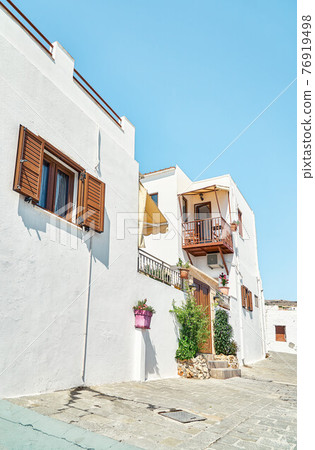 Narrow street with houses whitewashed walls and wooden shutters on windows 76919498