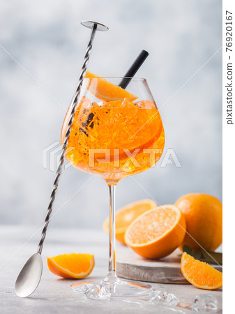 Glass of aperol spritz summer cocktail with oranges and bar spoon on light background.  76920167