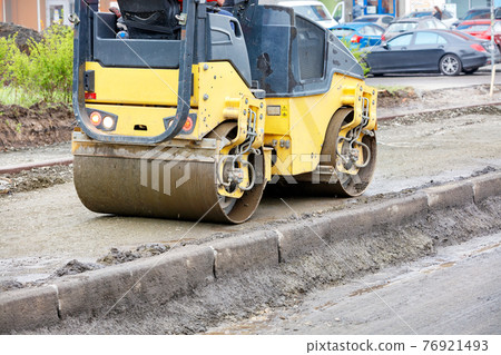 The compact road roller ramps the pavement foundation along the concrete curb and driveway. 76921493