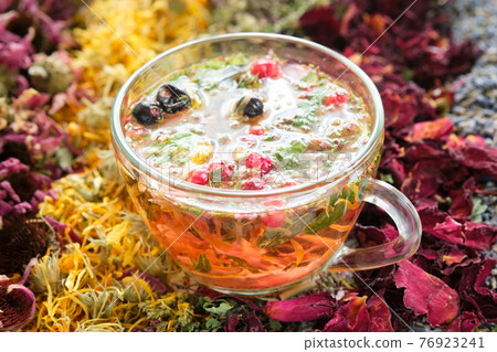 Glass cup of healthy tea with medicinal herbs and healthy berries. Dried echinacea, calendula, wild marjoram, rose petals on table. Alternative medicine. 76923241