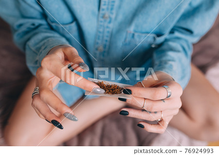 Woman wearing jeans shirt making hand rolled cigarette with tobacco at home Woman wearing jeans shirt making hand rolled cigarette with tobacco at home 76924993