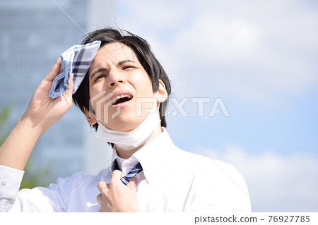 A young man who is hot and removes his mask and wipes his sweat with a handkerchief A young man who is hot and removes his mask and wipes his sweat with a handkerchief 76927785