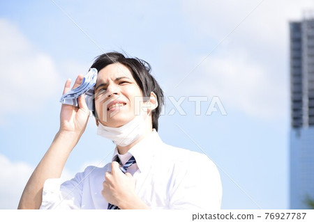 A young man who is hot and removes his mask and wipes his sweat with a handkerchief 76927787