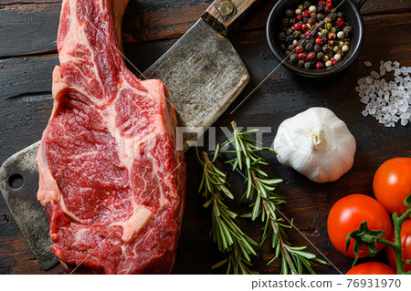Fresh tomahawk steak on meat cleaver. Organic farm marbled prime black angus beef. Dark wooden background. Top view. With seasonings, peppercorns, chilie, rosemary,salt,garlic. close up 76931970