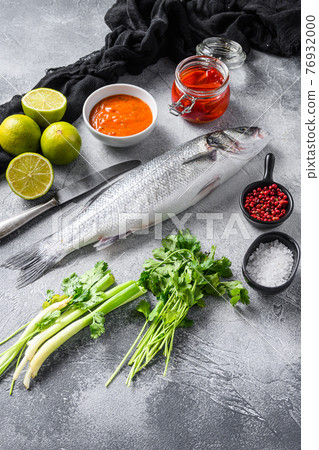Raw seabass with spices and herbs ingredients on grey concrete background side view. 76932000