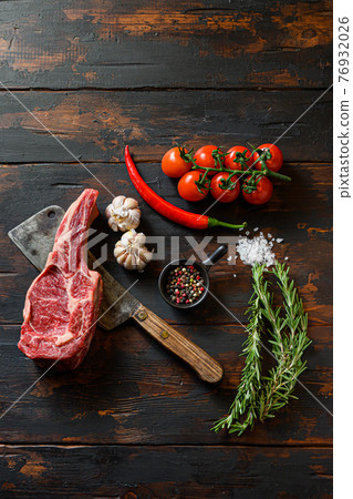 Raw Dallas steak on meat cleaver. Organic farm marbled prime black angus beef. Dark wooden background. top view. With seasonings, peppercorns, chilie rosemary,salt,garlic. Copyspace 76932026