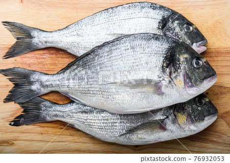 Raw dorada or sea bream fish set on chopping board with herbs for grill uncooked on white textured background side view. 76932053