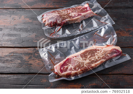 Vacuum packed meat , top blade beef steak on dark old wooden table, side view space for text. Vacuum packed meat , top blade beef steak on dark old wooden table, side view space for text. 76932518