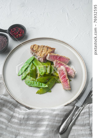 Sesame tuna steak grilled with spring onions and sugar snap peas, on plate, on white stone background 76932595