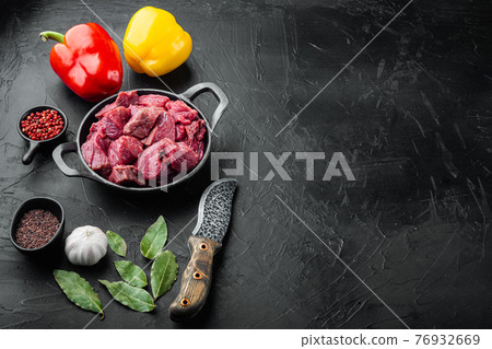 Raw meat diced for stew with sweet bell pepper, in cast iron frying pan, on black stone background, with copy space for text 76932669