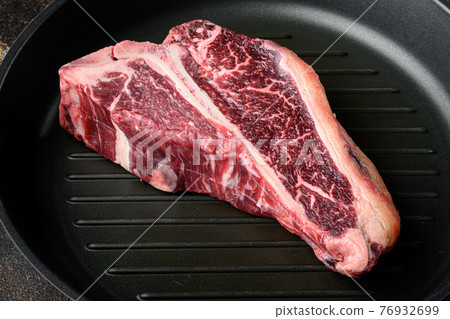 Dry aged t bone marbled beef steak, in frying cast iron pan, on old dark rustic background Dry aged t bone marbled beef steak, in frying cast iron pan, on old dark rustic background 76932699