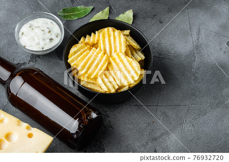 Crispy potato chips. Slices of potato, roasted with sea salt with Cheese and Onion, with dipping sauces , and bottle of beer , on gray stone background, with copy space for text Crispy potato chips. Slices of potato, roasted with sea salt with Cheese and Onion, with dipping sauces , and bottle of beer , on gray stone background, with copy space for text 76932720