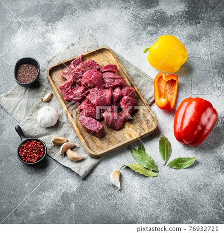 Fresh beef chunks served on table with ingredients ready for cooking with sweet bell pepper, on gray stone background, square format Fresh beef chunks served on table with ingredients ready for cooking with sweet bell pepper, on gray stone background, square format 76932721