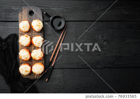 Baked sushi maki rolls with salmon, crab, cucumber, avocado, flying fish roe and spicy sauce, on black wooden table background, top view flat lay , with copyspace and space for text 76933565