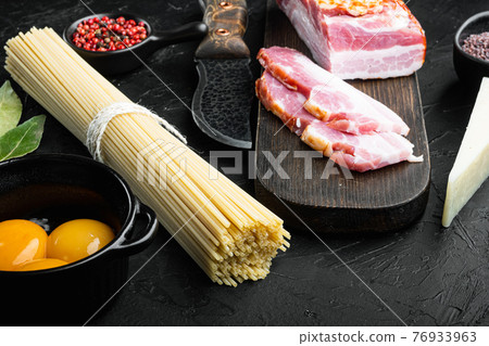 Ingredients for cooking Carbonara pasta, spaghetti with pancetta, egg and hard parmesan cheese., on black stone background 76933963