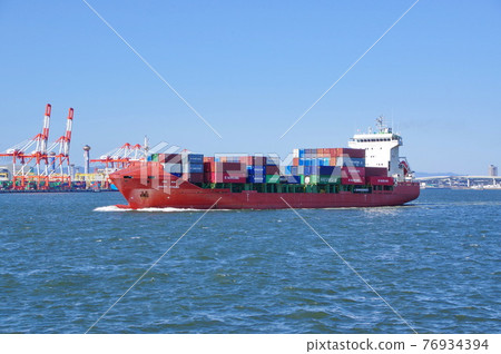 A red container ship leaving Osaka Port with white waves 76934394