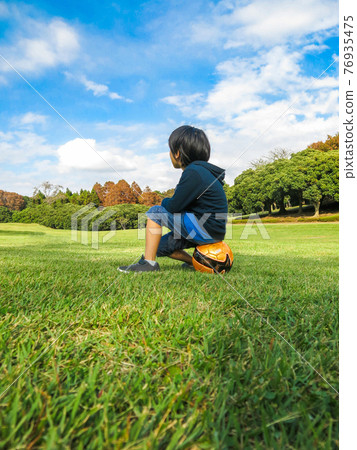 足球男孩坐在草地上的一個球在陽光明媚的一天 足球男孩坐在草地上的一個球在陽光明媚的一天 76935475