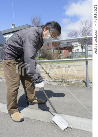 Senior man picking up a littering mask 76936621