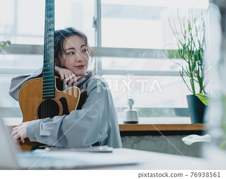 Young woman holding a guitar by the window Young woman holding a guitar by the window 76938561