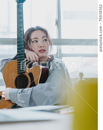 Young woman holding a guitar by the window Young woman holding a guitar by the window 76938562