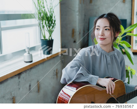 Young woman holding a guitar by the window 76938567