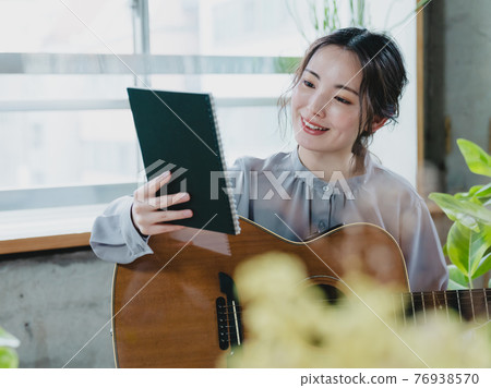 A young woman composing with a guitar by the window A young woman composing with a guitar by the window 76938570