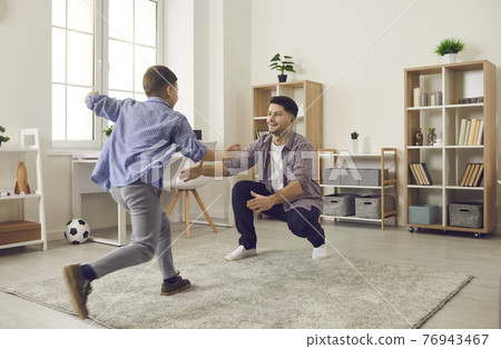 Happy little son running to hug his daddy while having fun time at home together 76943467