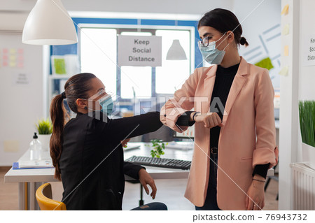 Woman colleagues wearing protective face mask greeting bumping elbows Woman colleagues wearing protective face mask greeting bumping elbows 76943732