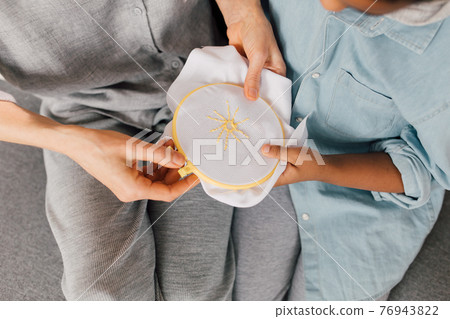 Boy looking at the embroidery while his grandmother sitting at the sofa Boy looking at the embroidery while his grandmother sitting at the sofa 76943822