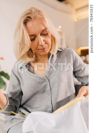 Woman doing some needlework while sitting at the sofa with hoops and canvas Woman doing some needlework while sitting at the sofa with hoops and canvas 76943835