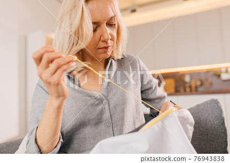Female sitting at the sofa with embroidery, hoop and needle at the room Female sitting at the sofa with embroidery, hoop and needle at the room 76943838